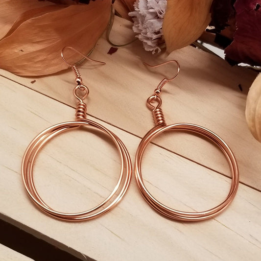 Rose gold hoop earrings on a wooden surface with flowers in the background