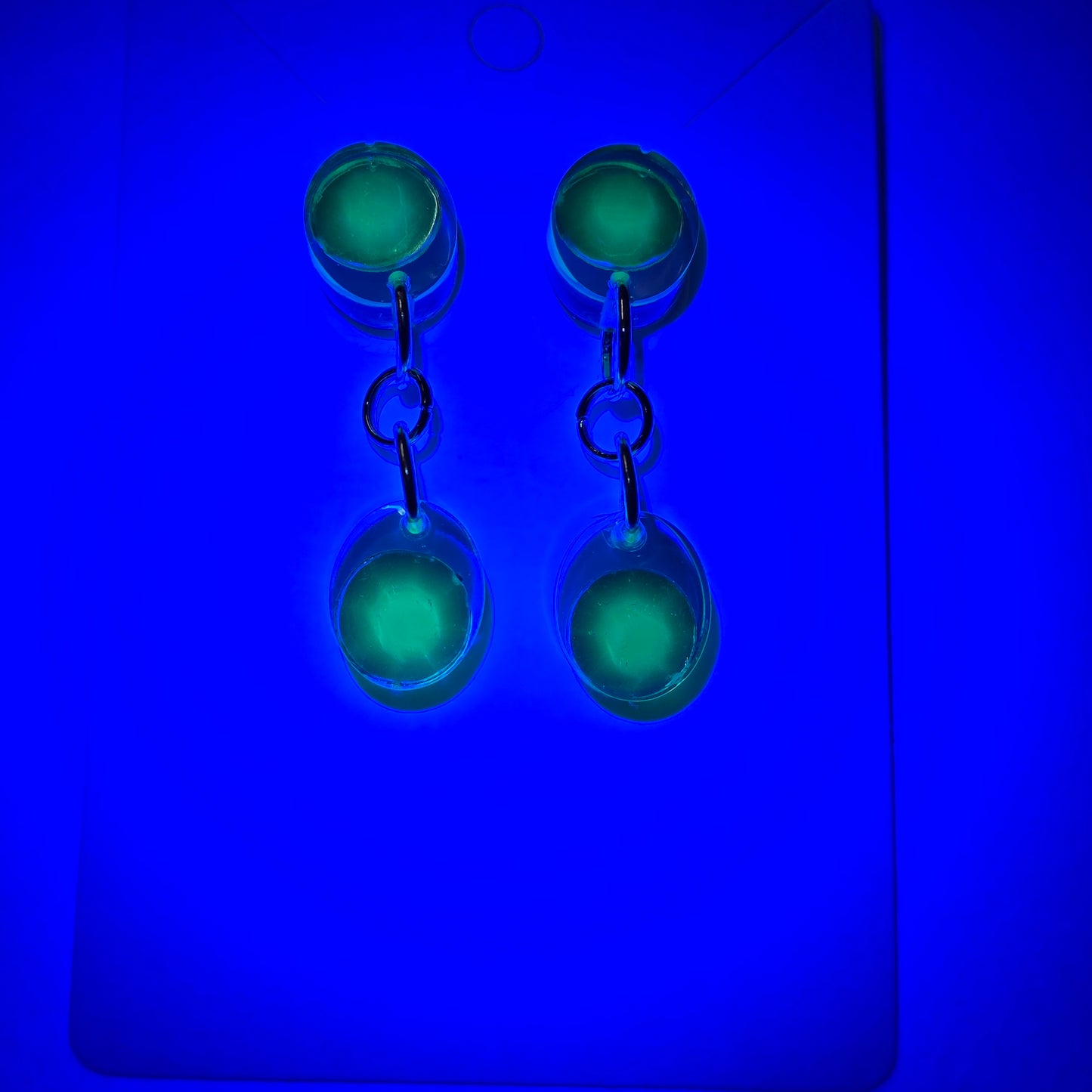 Set of three green glass objects with metal clasps on a blue background