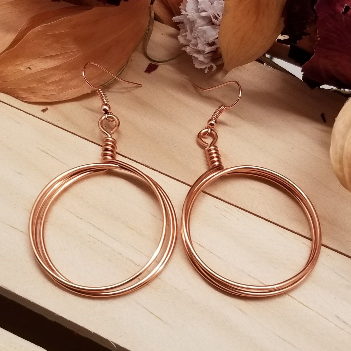 Rose gold hoop earrings on a wooden surface with flowers in the background
