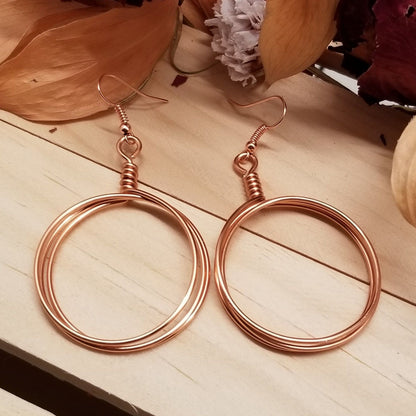Rose gold hoop earrings on a wooden surface with flowers in the background