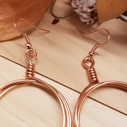 Rose gold hoop earrings on a wooden surface with flowers in the background