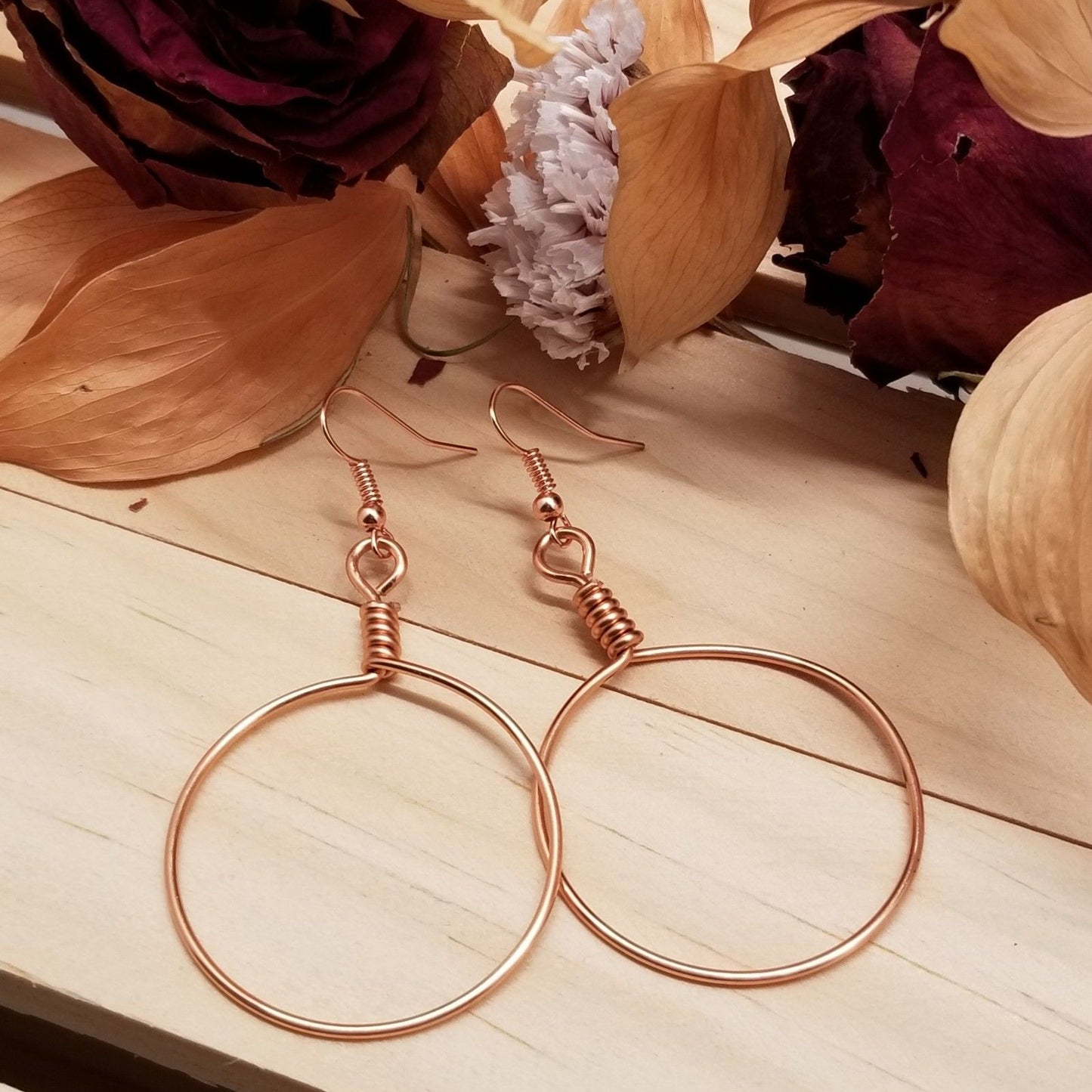 Rose gold hoop earrings on a wooden surface with dried flowers in the background