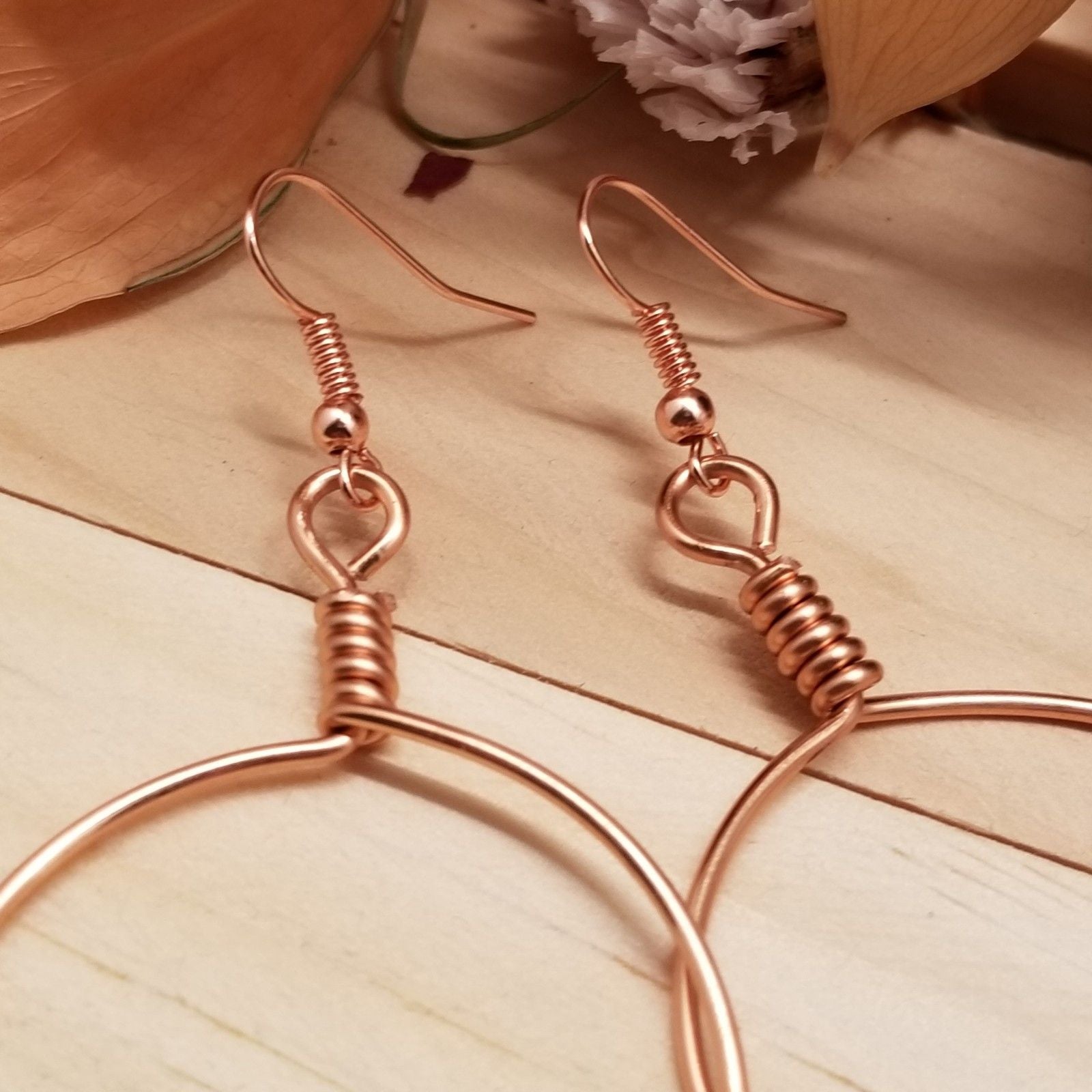 Rose gold hoop earrings on a wooden surface with a soft focus background