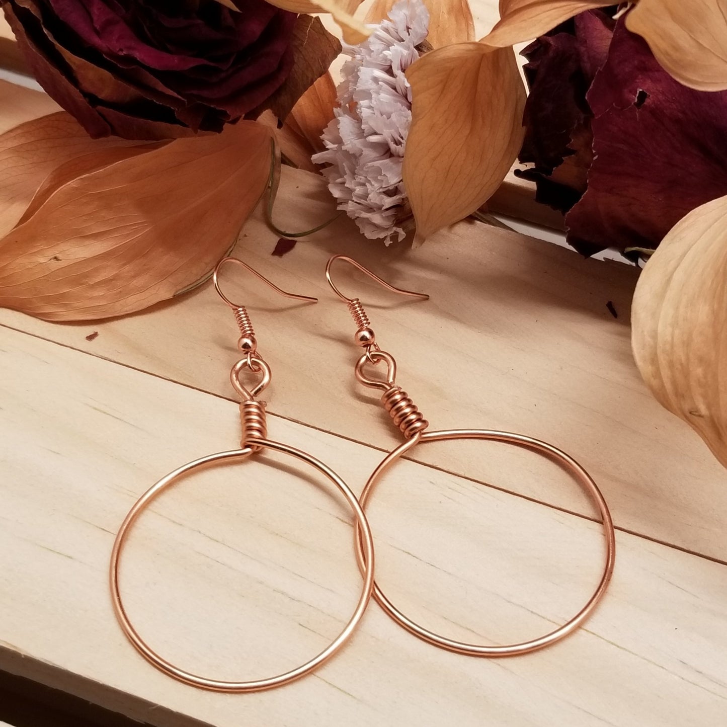 Rose gold hoop earrings on a wooden surface with dried flowers.
