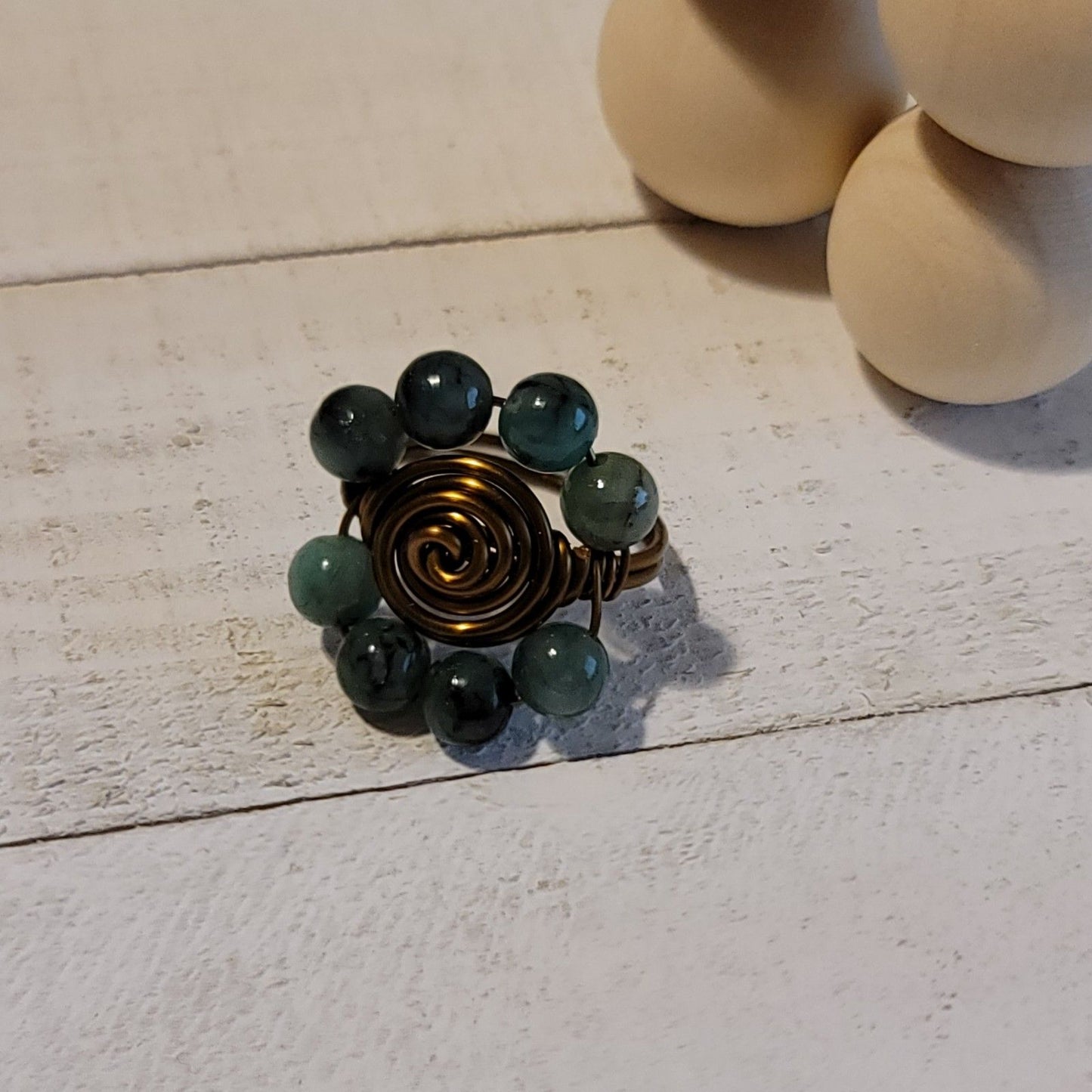 Ring with green beads and bronze spiral on a light wooden surface
