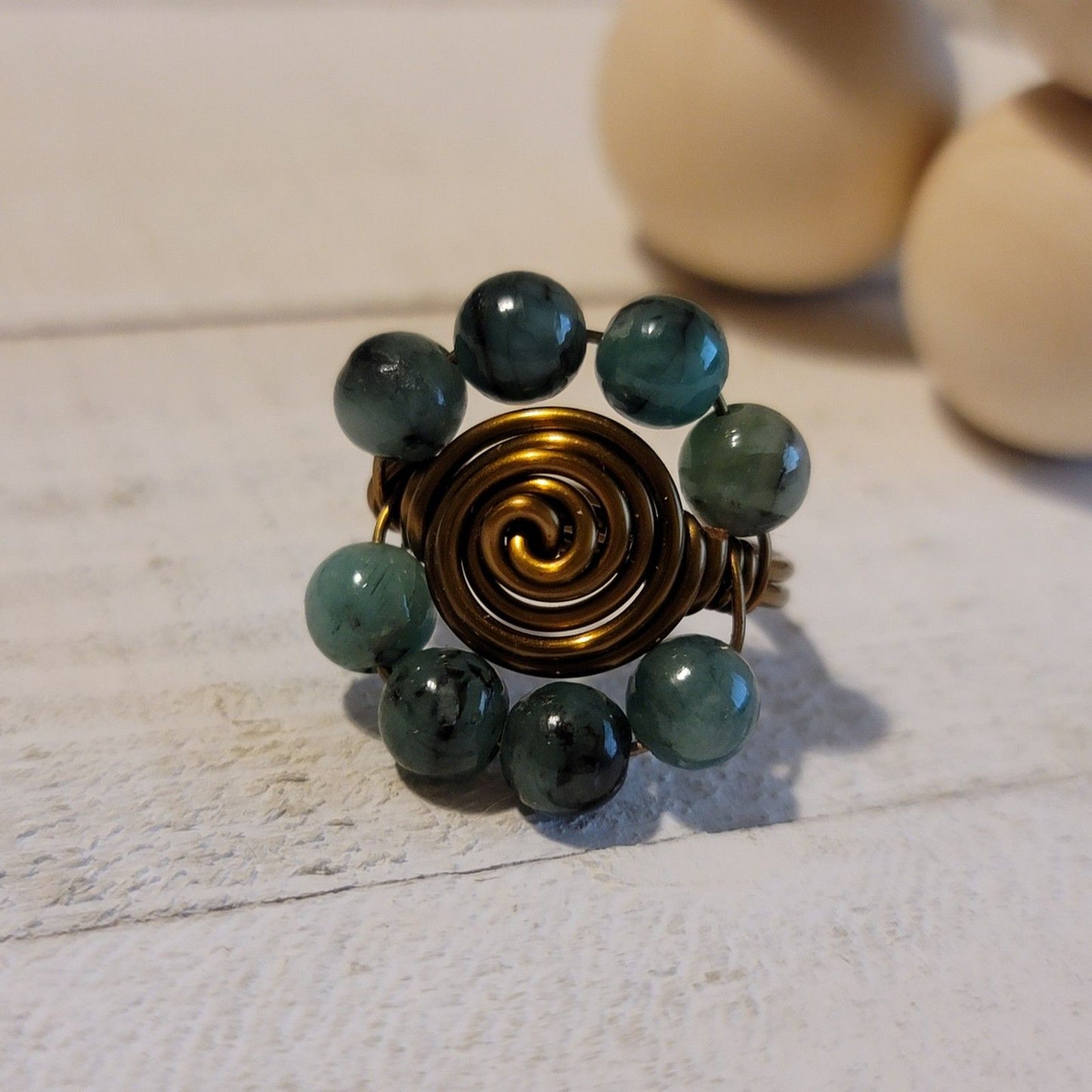Ring with green beads and gold spiral design on a textured surface