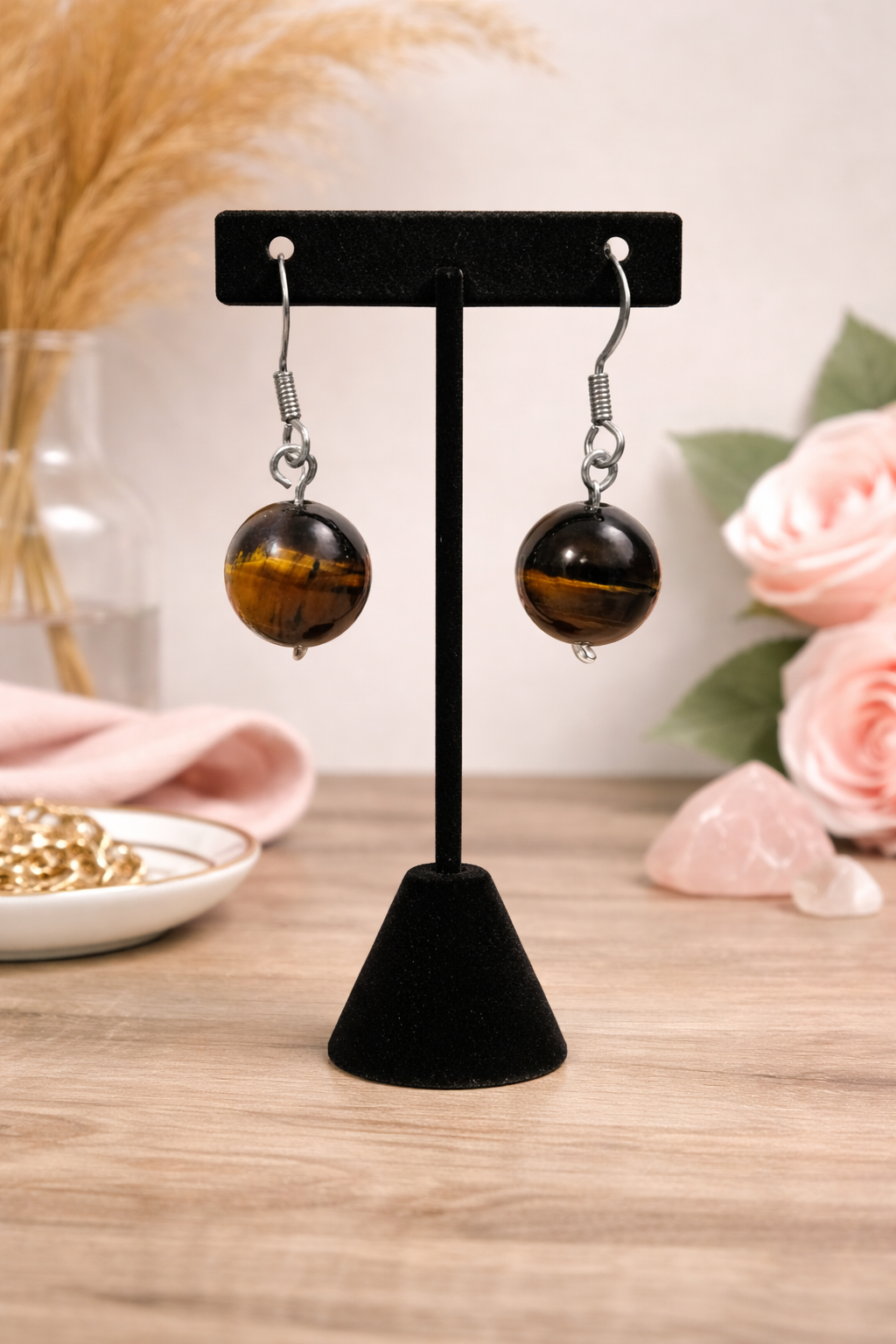 Black spherical earrings on a black stand with a blurred background of flowers and jewelry.