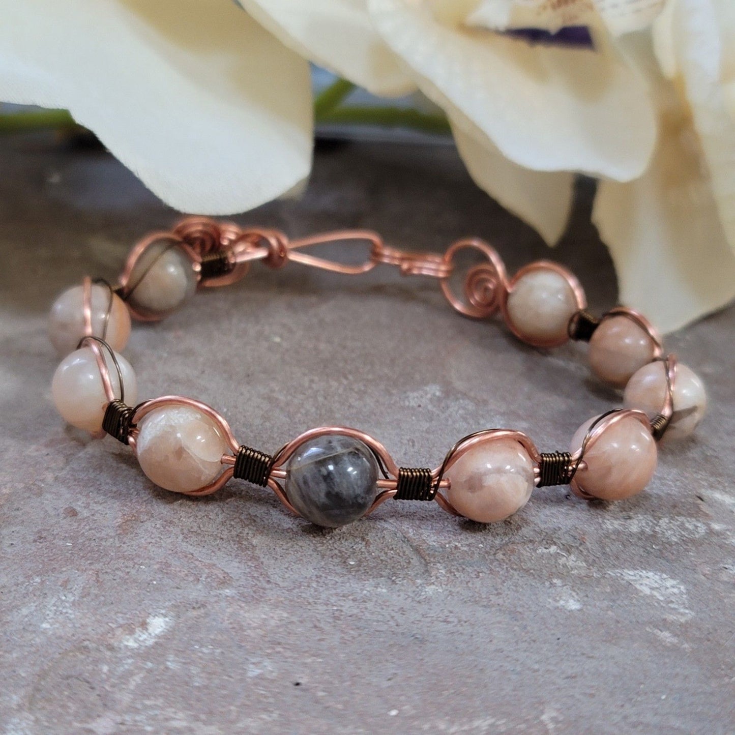 Bracelet with pink and gray beads on a stone surface with flowers in the background