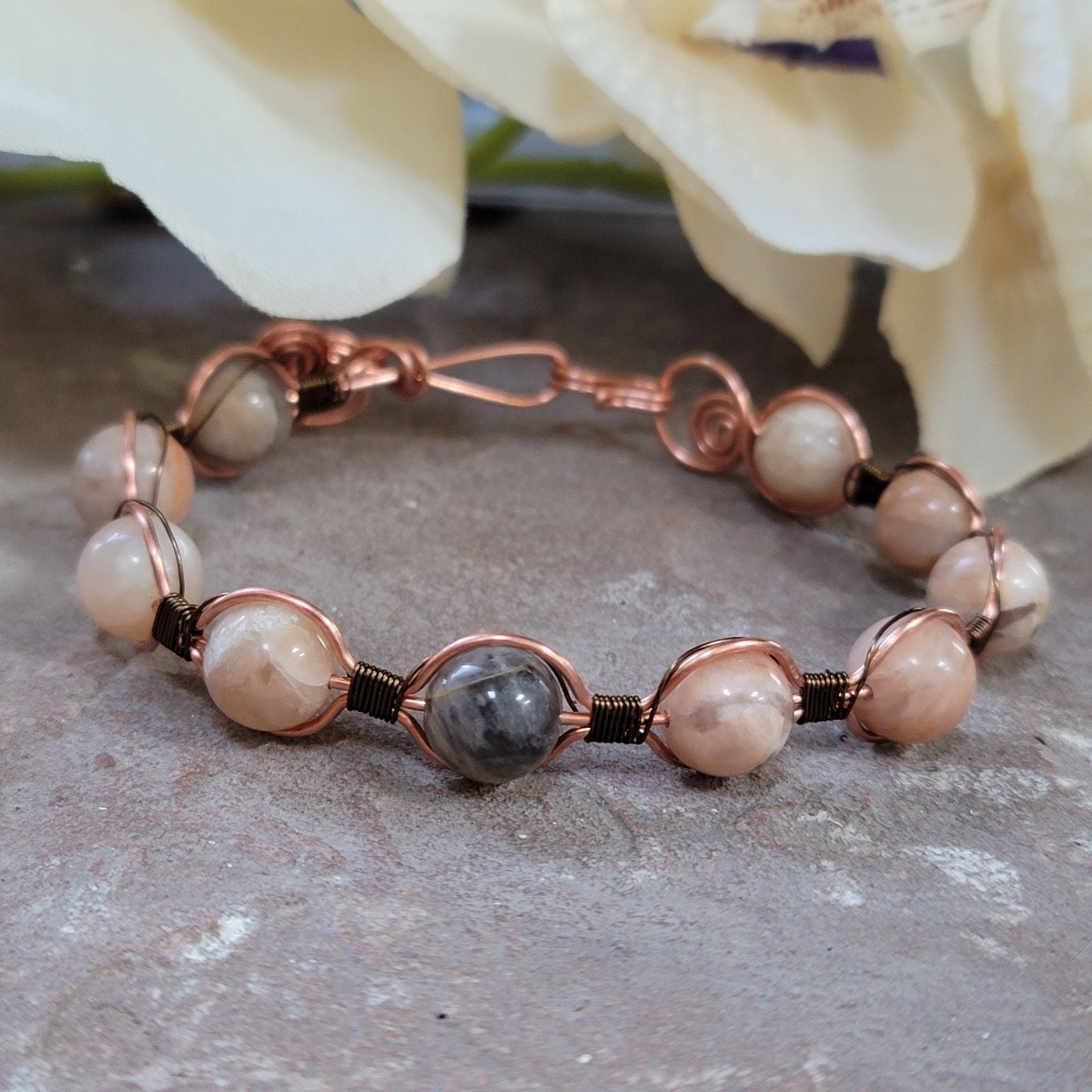 Bracelet with pink and gray beads on a stone surface with flowers in the background