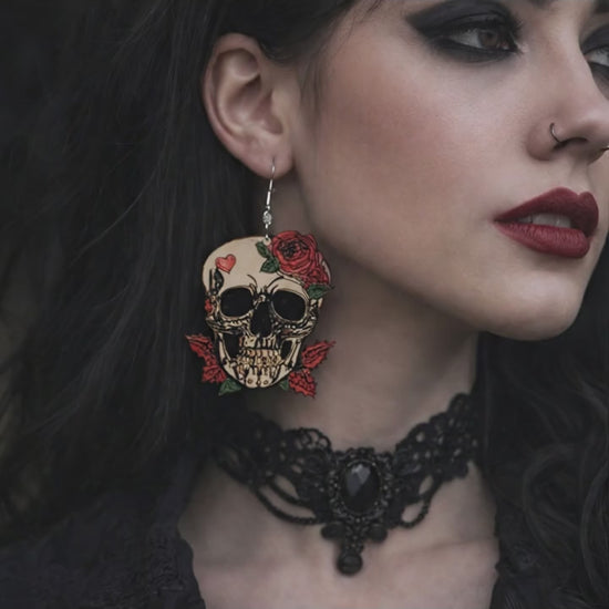 A close-up video of a woman in gothic attire; she slightly turns her head, causing her large skull-and-rose earring to sway gently against her dark, wavy hair.