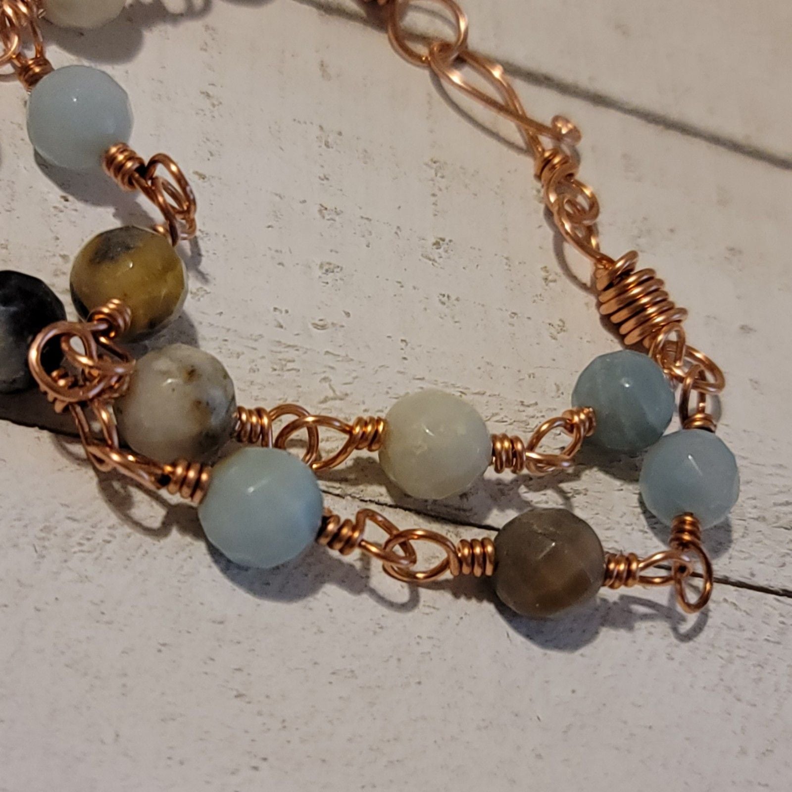 Bracelet with copper wire wrapping and natural stone beads on a light wooden surface