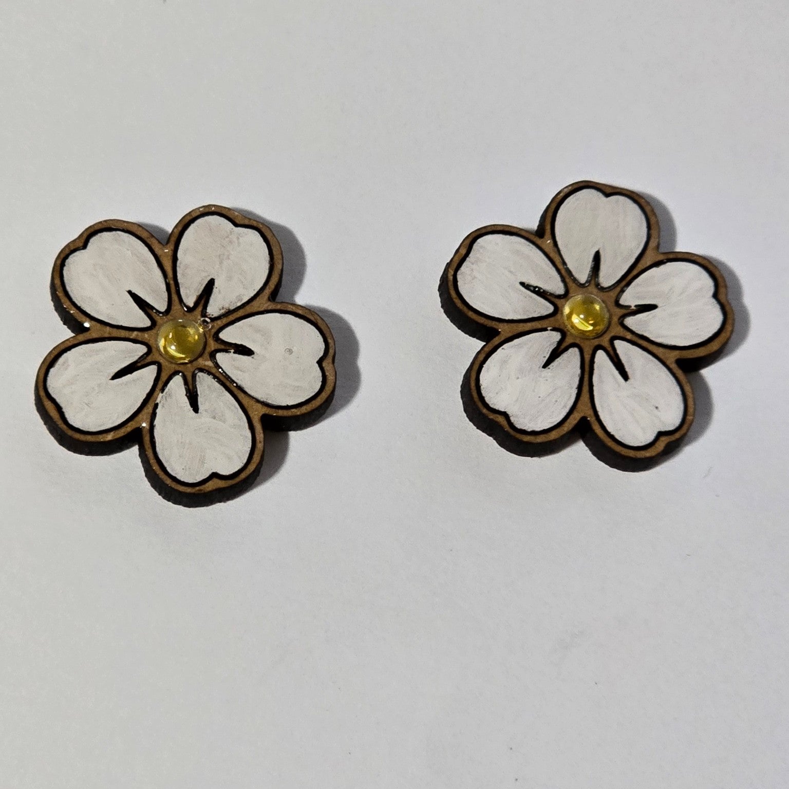 Flower-shaped earrings with white centers and gold accents on a light gray background
