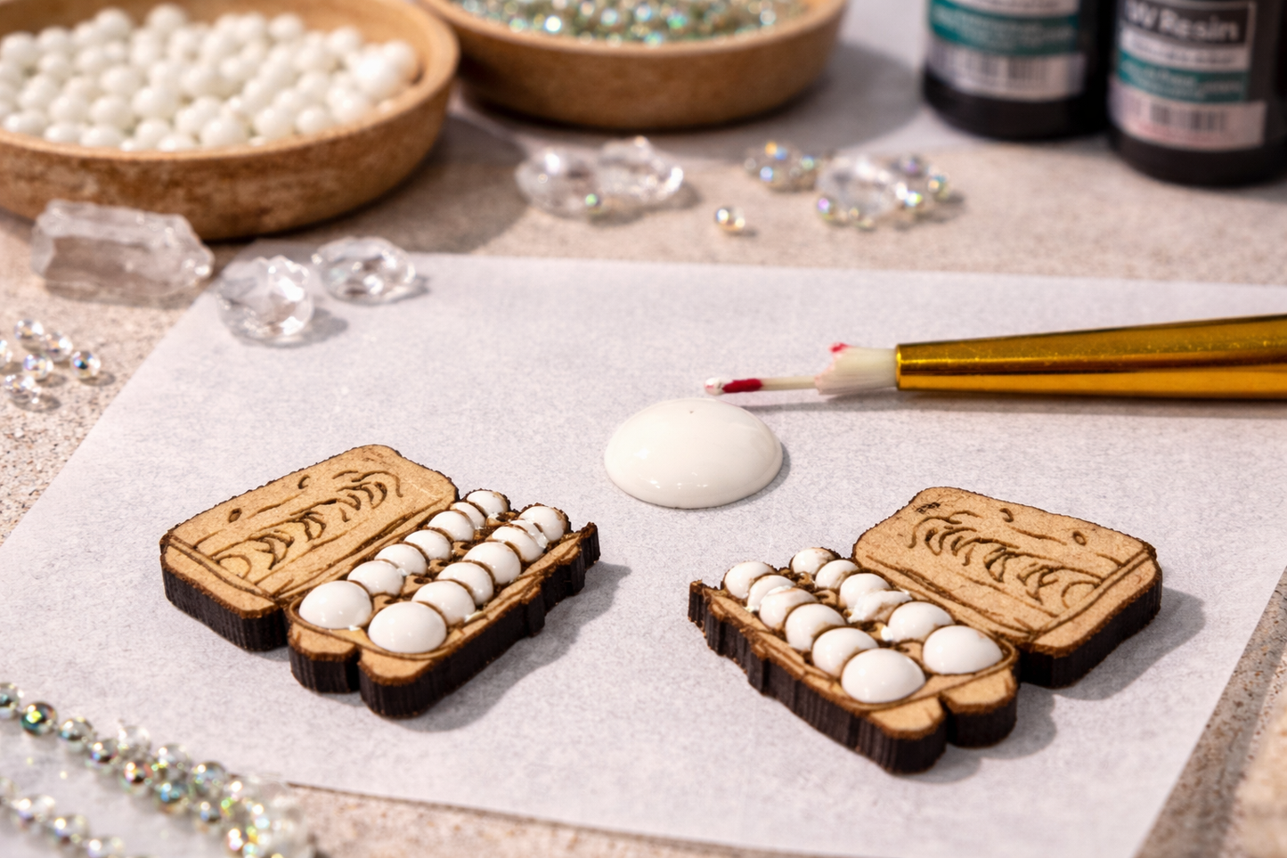 Wooden jewelry molds with white beads on a table with paint and tools.