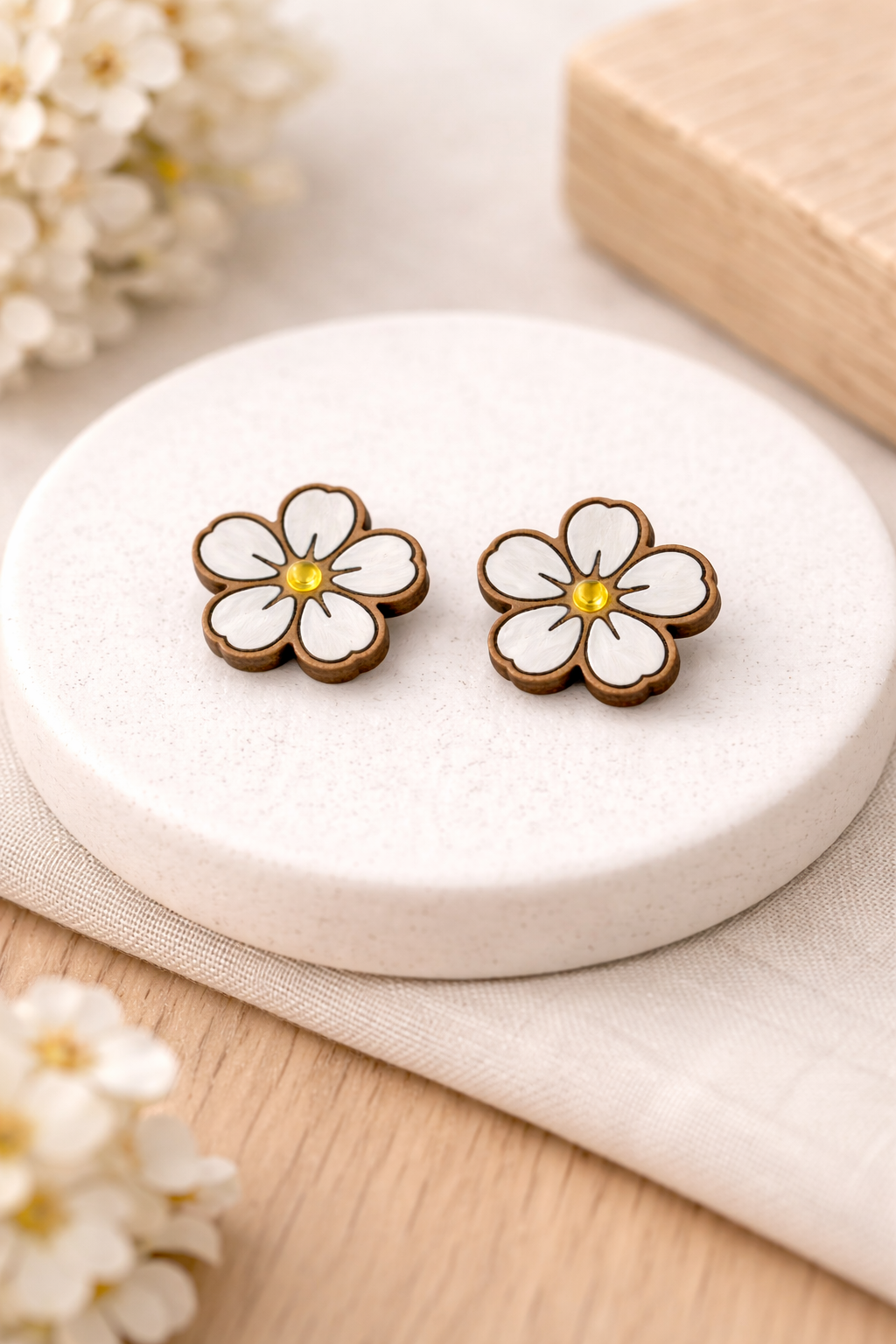 Flower-shaped earrings on a white stone with a wooden box in the background