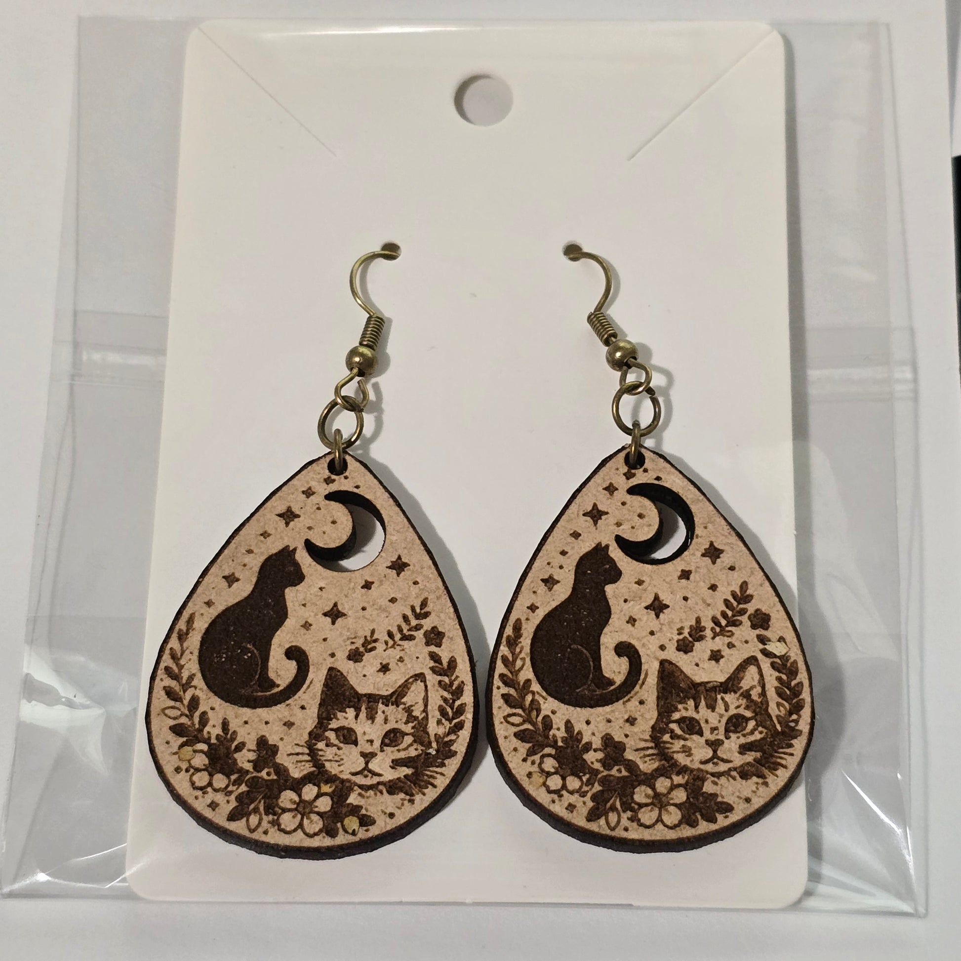 Teardrop-shaped earrings with cat and moon design on a clear card.