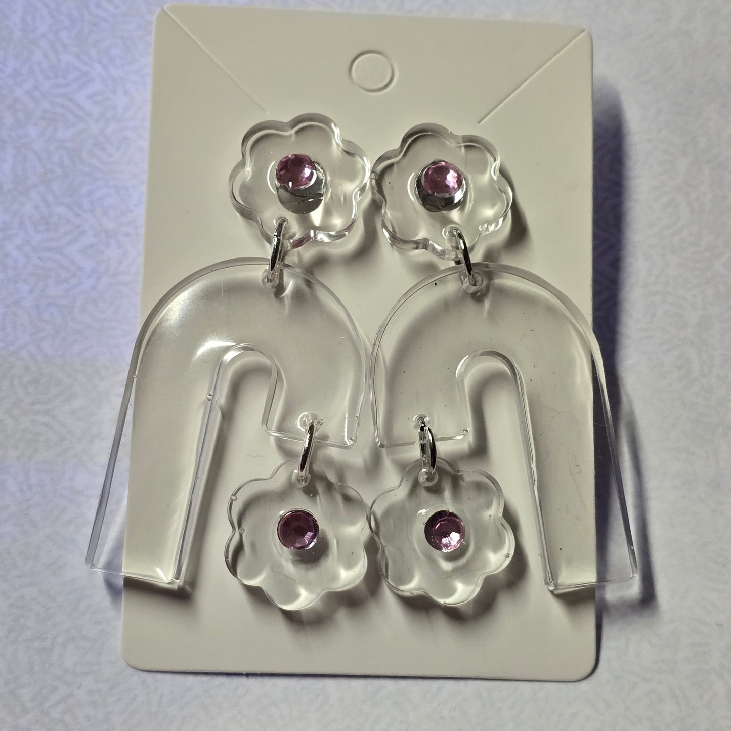 Flower-shaped earrings with purple stones on a clear display card against a white background