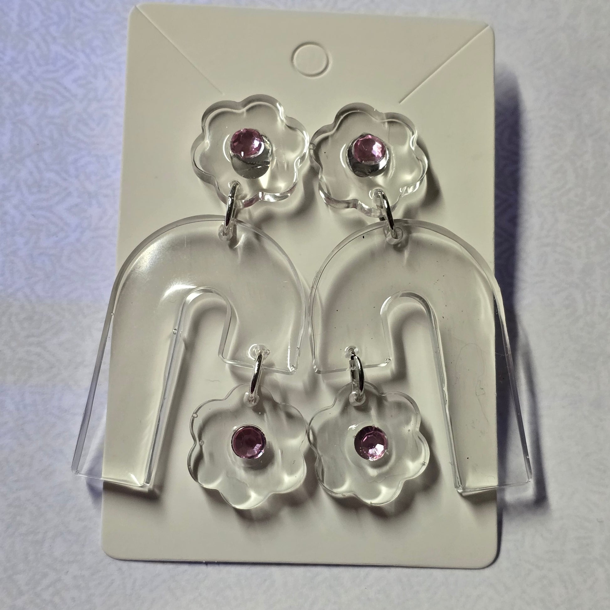 Flower-shaped earrings with purple stones on a clear display card against a white background