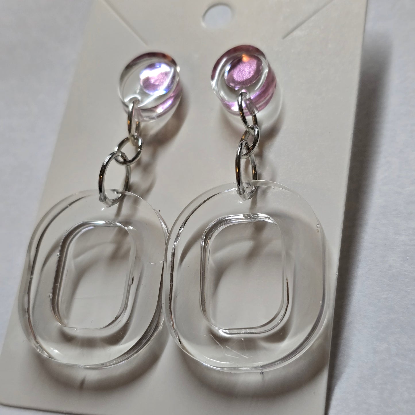 Clear plastic earring display with pink gemstones on a white background