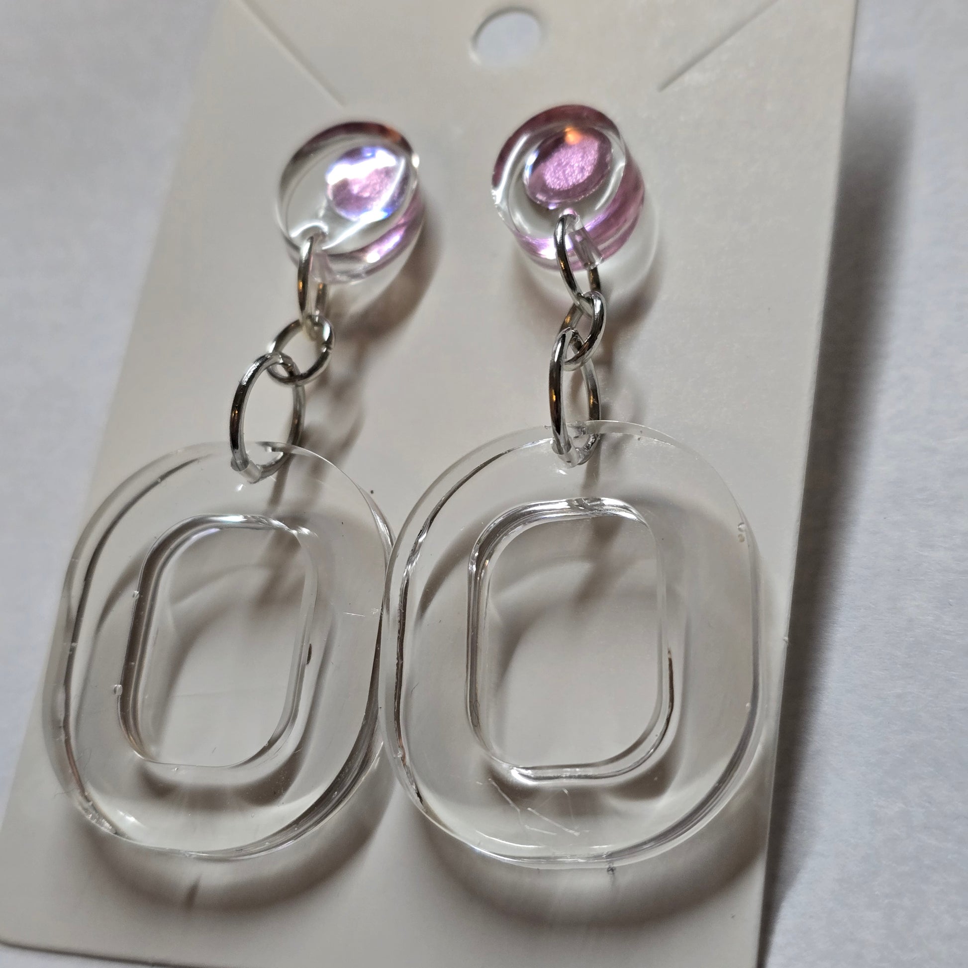 Clear plastic earring display with pink gemstones on a white background