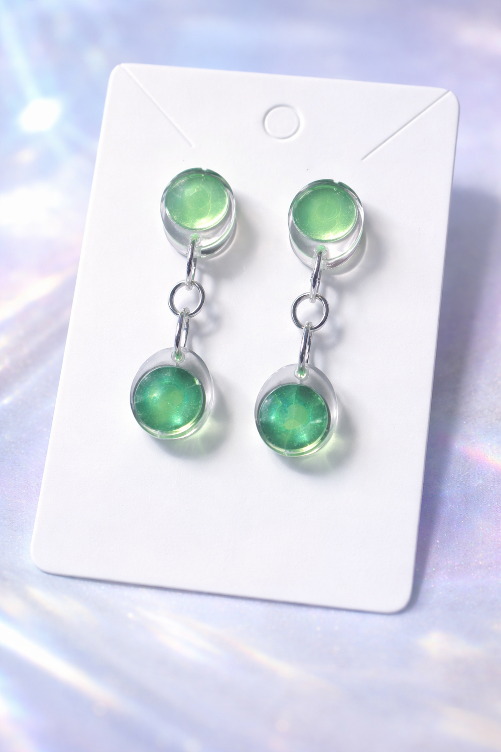 Pair of green earrings on a white card with a light purple background