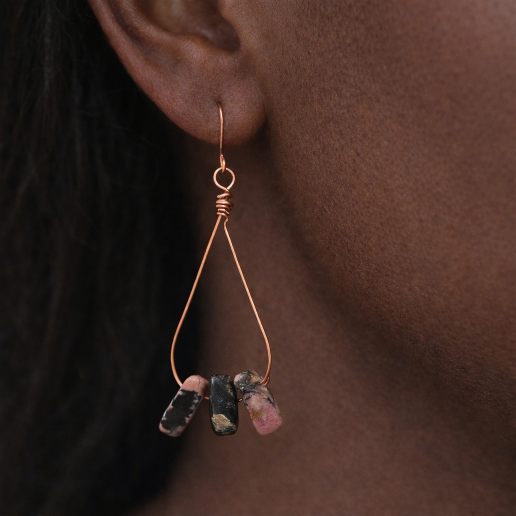 Earring with three dangling stones worn by a person against a brown background
